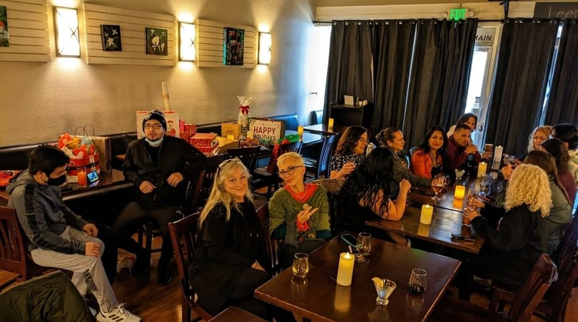 A group of people gathered at tables in a restaurant, celebrating with drinks and gifts.
